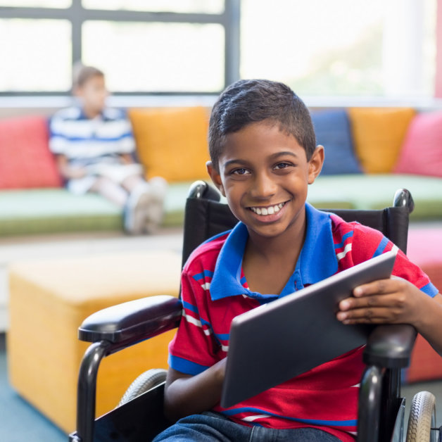 Portrait of disabled schoolboy on wheelchair using digital tablet in library at school